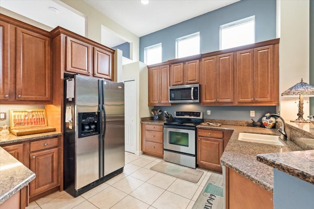 kitchen with light tile patterned floors, stainless steel appliances, sink, and stone counters