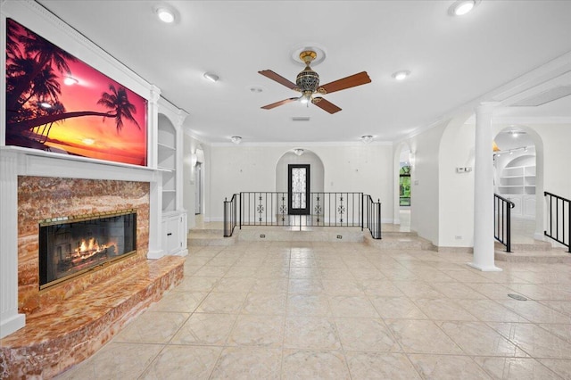 unfurnished living room with ceiling fan, a premium fireplace, crown molding, and built in shelves