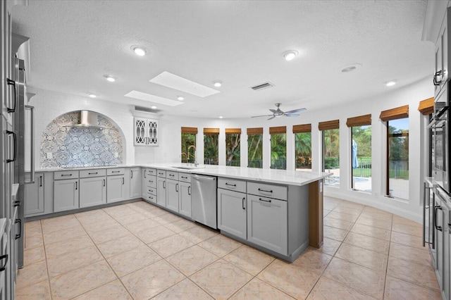 kitchen with kitchen peninsula, appliances with stainless steel finishes, a skylight, sink, and gray cabinets