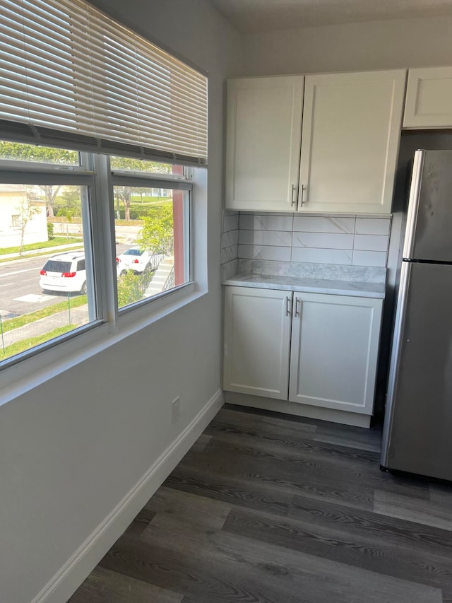 kitchen with tasteful backsplash, white cabinetry, dark hardwood / wood-style flooring, and stainless steel refrigerator