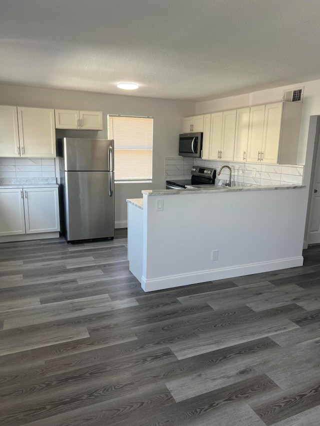 kitchen with stainless steel appliances, kitchen peninsula, white cabinets, and tasteful backsplash