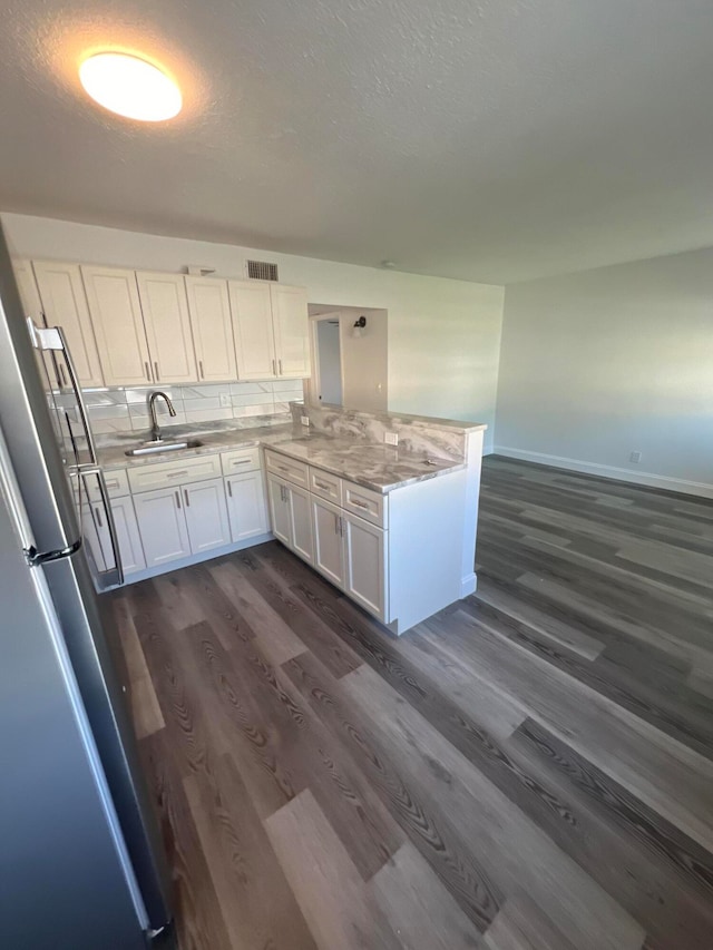 kitchen featuring dark wood-type flooring, stainless steel refrigerator, sink, decorative backsplash, and white cabinetry