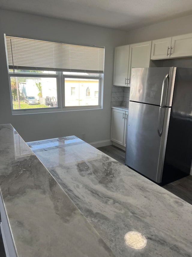 kitchen featuring white cabinets, light stone counters, stainless steel refrigerator, and a healthy amount of sunlight