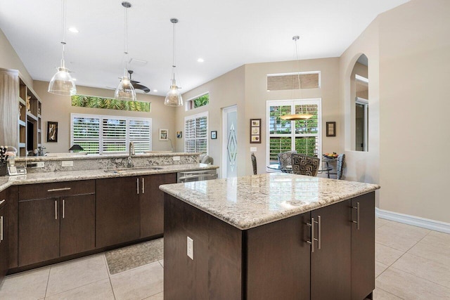 kitchen featuring light stone counters, a kitchen island, sink, and hanging light fixtures