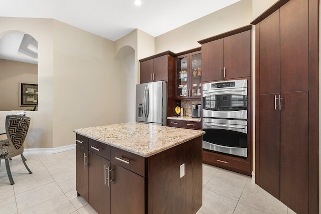 kitchen featuring a center island, stainless steel appliances, dark brown cabinetry, and light stone countertops