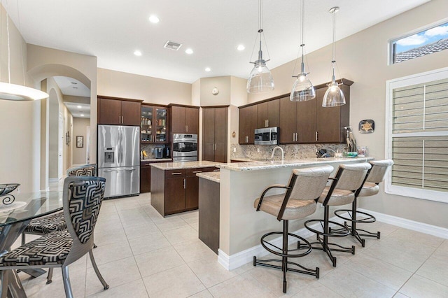 kitchen featuring decorative light fixtures, light stone counters, stainless steel appliances, dark brown cabinets, and tasteful backsplash