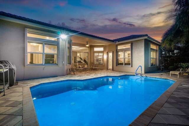 pool at dusk featuring ceiling fan and a patio area