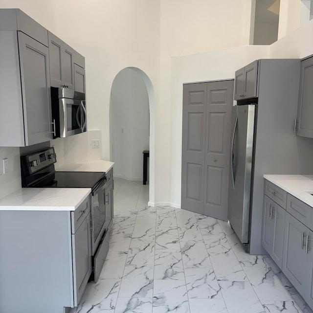 kitchen featuring gray cabinets, a high ceiling, stainless steel appliances, and tasteful backsplash