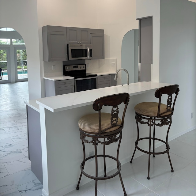 kitchen featuring kitchen peninsula, appliances with stainless steel finishes, a kitchen bar, gray cabinetry, and sink