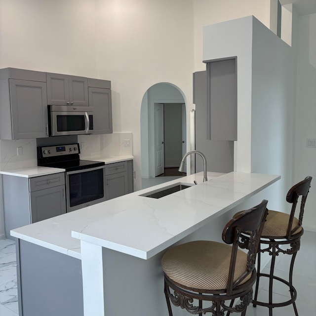 kitchen with sink, gray cabinetry, stainless steel appliances, and kitchen peninsula