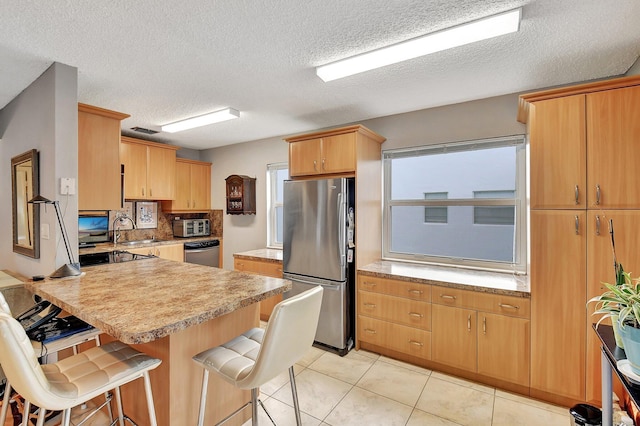 kitchen featuring a breakfast bar area, stainless steel appliances, light tile patterned flooring, and a textured ceiling