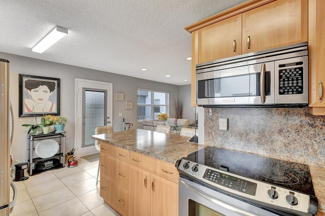 kitchen featuring light brown cabinetry, appliances with stainless steel finishes, light tile patterned flooring, decorative backsplash, and a textured ceiling