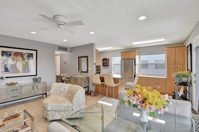 living room with a textured ceiling, light tile patterned flooring, and ceiling fan