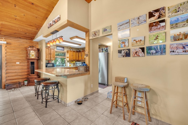 kitchen with light tile patterned flooring, kitchen peninsula, stainless steel refrigerator, and a kitchen breakfast bar