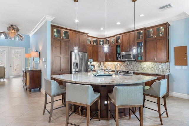 kitchen with hanging light fixtures, stainless steel appliances, ornamental molding, and a kitchen island with sink