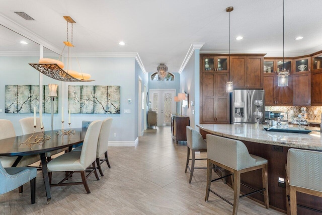 kitchen featuring ornamental molding, tasteful backsplash, light stone countertops, hanging light fixtures, and stainless steel refrigerator with ice dispenser