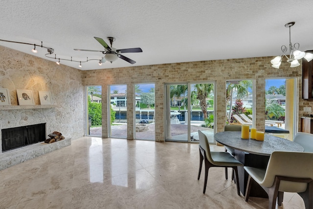 dining area with track lighting, ceiling fan with notable chandelier, a textured ceiling, and a premium fireplace