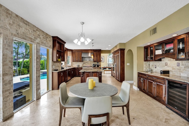 dining area with a textured ceiling, beverage cooler, an inviting chandelier, and sink