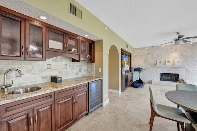 kitchen featuring sink, wine cooler, a stone fireplace, rail lighting, and ceiling fan