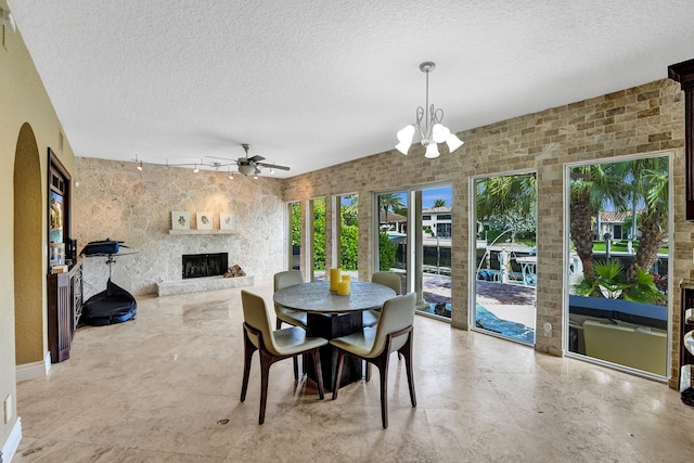 dining area with a large fireplace and ceiling fan with notable chandelier