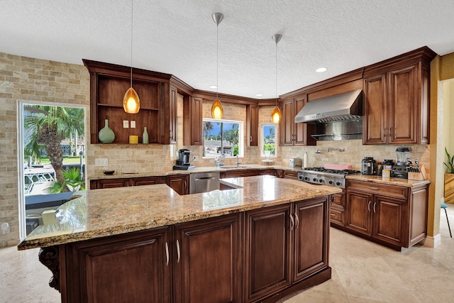 kitchen with a textured ceiling, a kitchen island, light stone countertops, hanging light fixtures, and wall chimney range hood