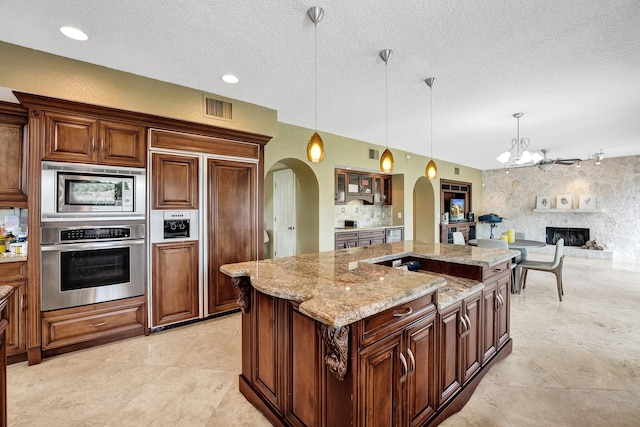 kitchen with pendant lighting, built in appliances, a textured ceiling, an island with sink, and light stone countertops