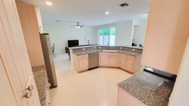 kitchen with light brown cabinets, sink, kitchen peninsula, appliances with stainless steel finishes, and dark stone counters