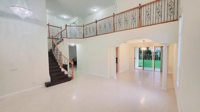 stairway featuring a notable chandelier, a towering ceiling, and ornate columns