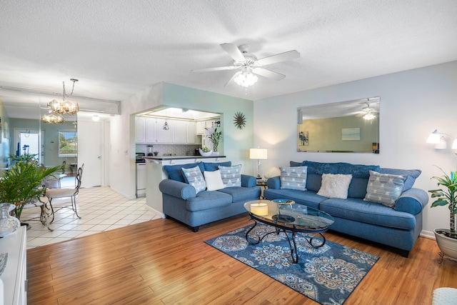 living room with ceiling fan with notable chandelier, a textured ceiling, and light hardwood / wood-style floors