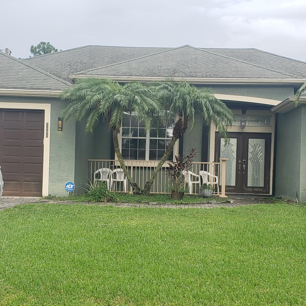view of exterior entry featuring a yard, stucco siding, a garage, and french doors