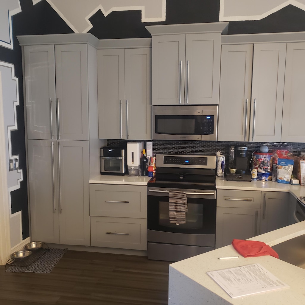 kitchen featuring stainless steel appliances, light countertops, dark wood finished floors, backsplash, and vaulted ceiling