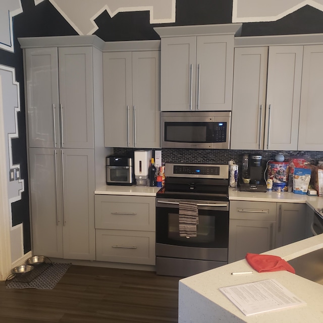 kitchen featuring stainless steel appliances, light countertops, dark wood finished floors, backsplash, and vaulted ceiling