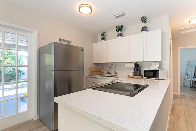 kitchen featuring stainless steel fridge, light stone countertops, sink, white cabinetry, and light wood-type flooring