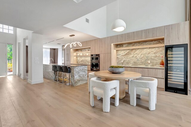 dining space featuring light wood-type flooring, sink, wine cooler, and a towering ceiling