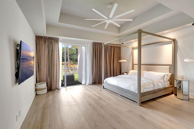 unfurnished bedroom with a tray ceiling, ceiling fan, access to outside, and light hardwood / wood-style flooring