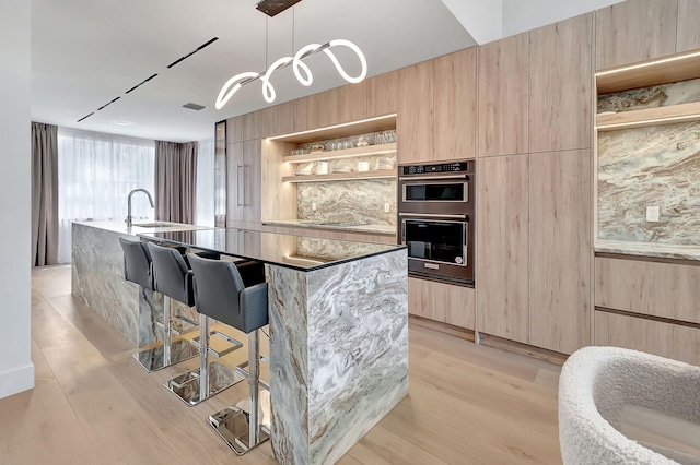 kitchen featuring decorative light fixtures, a breakfast bar area, an island with sink, and light hardwood / wood-style floors