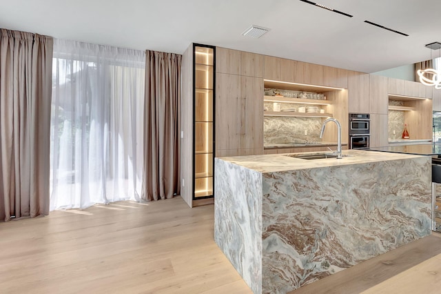 kitchen featuring a center island with sink, hanging light fixtures, a wealth of natural light, and light wood-type flooring