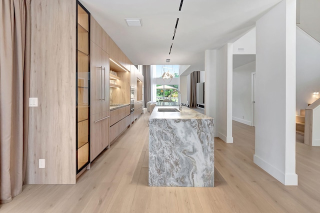 kitchen with light hardwood / wood-style flooring, light stone counters, sink, an island with sink, and pendant lighting