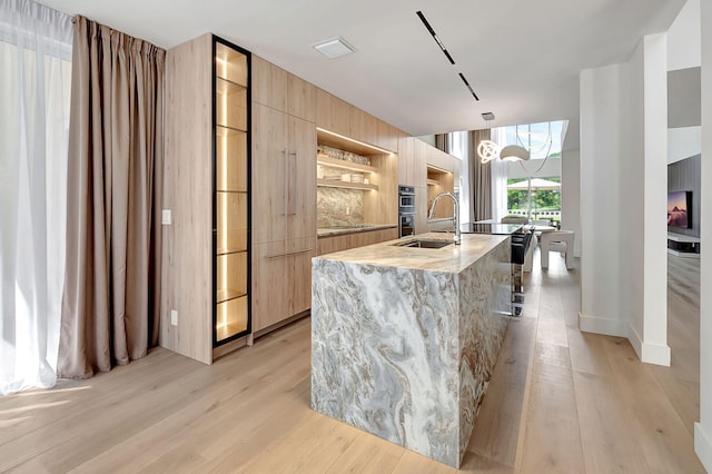 kitchen with a kitchen island with sink, light wood-type flooring, decorative light fixtures, light stone counters, and an inviting chandelier