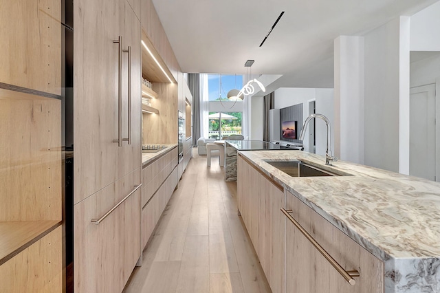 kitchen featuring a center island with sink, hanging light fixtures, sink, light stone counters, and light wood-type flooring