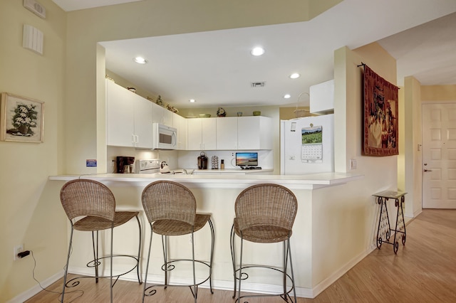 kitchen featuring white cabinets, white appliances, a kitchen breakfast bar, and light hardwood / wood-style floors