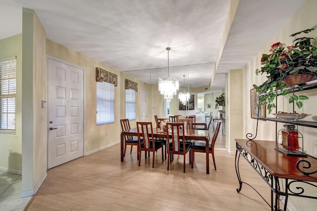 dining area with a textured ceiling, a notable chandelier, and light hardwood / wood-style flooring