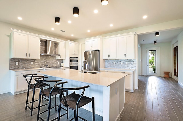 kitchen featuring stainless steel appliances, wall chimney exhaust hood, white cabinets, and a kitchen island with sink