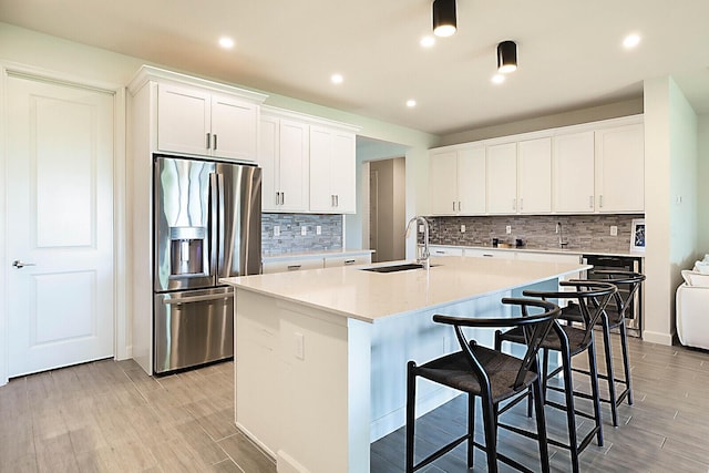 kitchen featuring white cabinetry, light hardwood / wood-style floors, sink, stainless steel fridge, and a kitchen island with sink