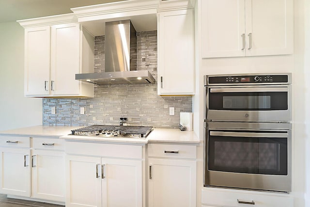 kitchen with appliances with stainless steel finishes, backsplash, white cabinetry, and wall chimney range hood