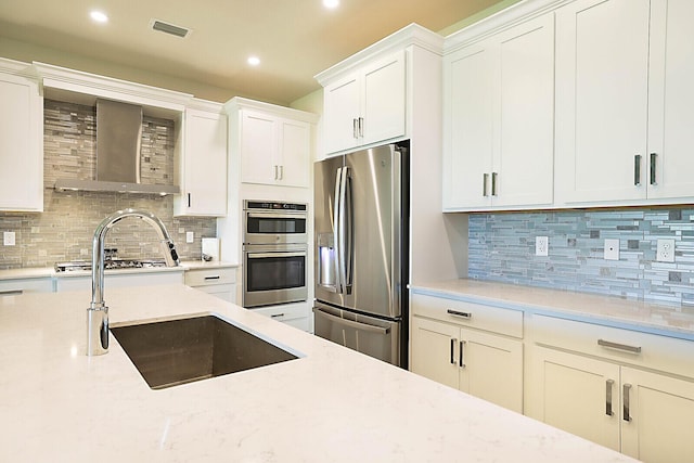 kitchen with white cabinets, appliances with stainless steel finishes, wall chimney exhaust hood, decorative backsplash, and sink