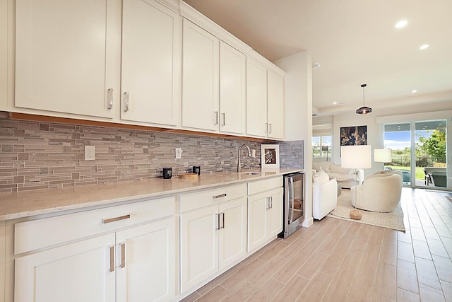 kitchen with wine cooler, backsplash, sink, light stone countertops, and white cabinets