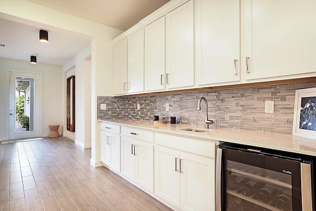 kitchen featuring beverage cooler, white cabinetry, tasteful backsplash, sink, and light hardwood / wood-style flooring