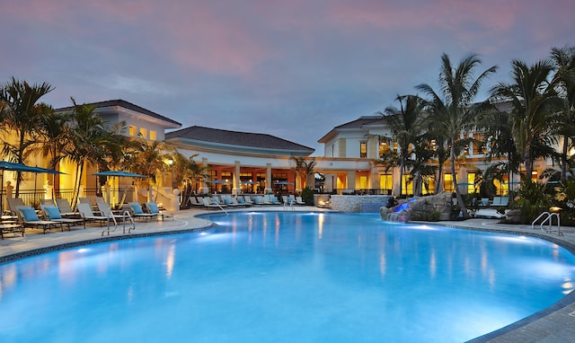 pool at dusk featuring pool water feature and a patio