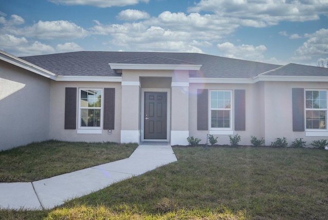 view of front of home featuring roof with shingles, a front lawn, and stucco siding